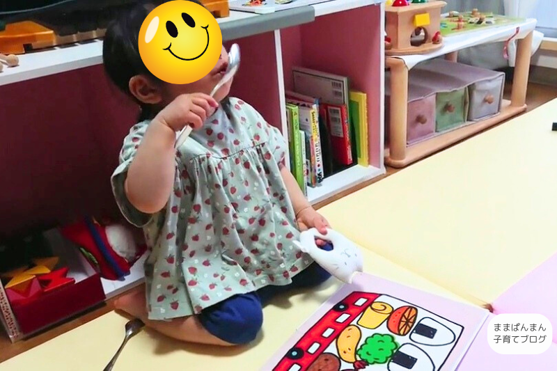 絵本を読みながらスプーンで食べる真似をしている子ども